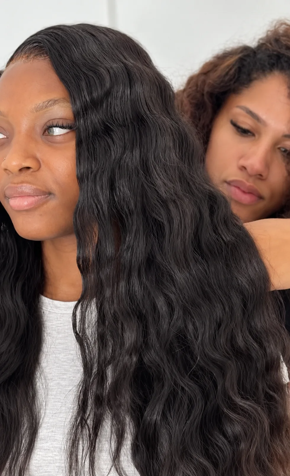 Client with long black waves while a stylist works behind her